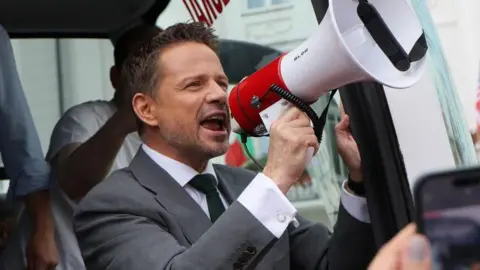 EPA Rafal Trzaskowski wears a suit, stands in a bus doorway, holds up a megaphone and speaks into it