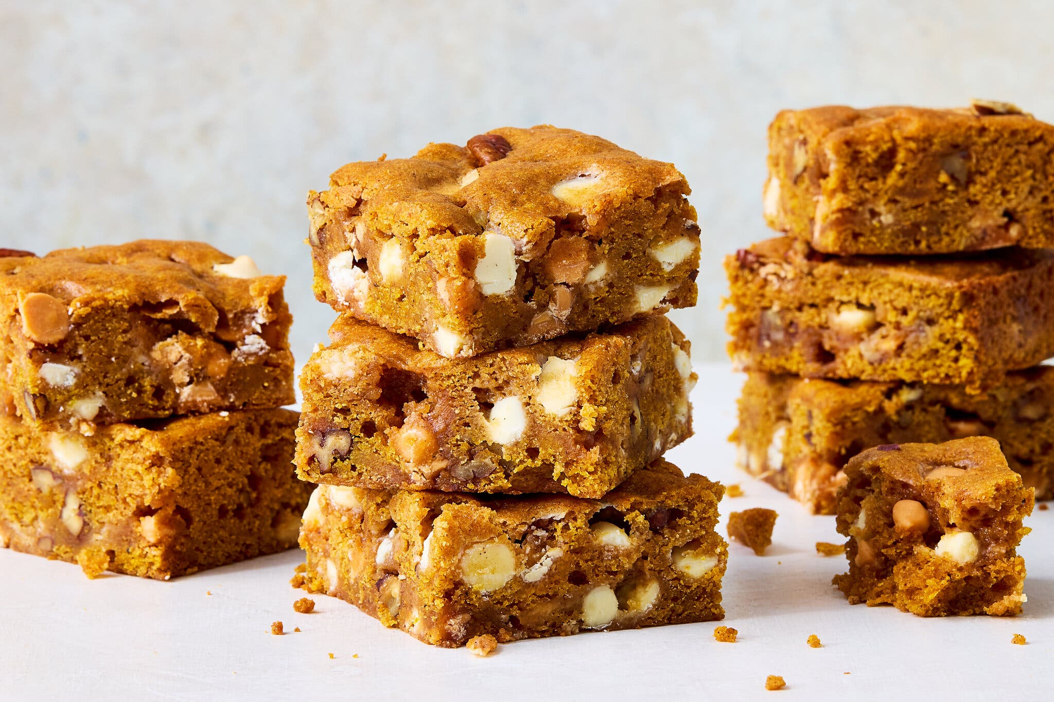 A stack of pumpkin blondies with white chocolate and nuts, against a blurred gray background.