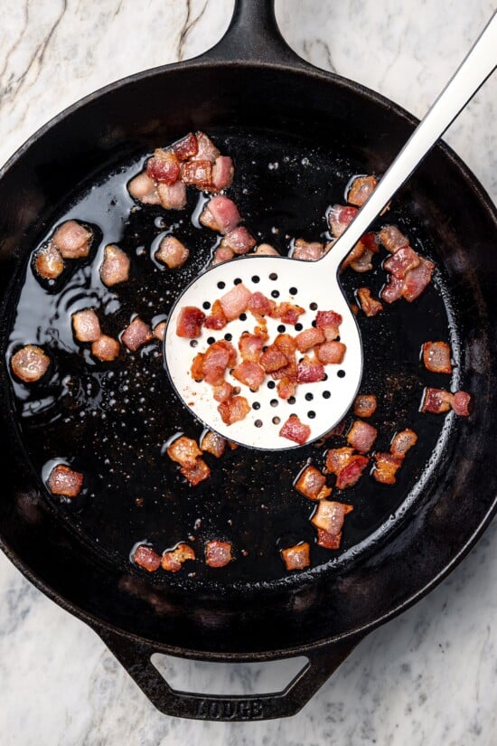 This Slow Cooker Coq au Vin is easier and lighter than the traditional version, but just as delicious with smoky bacon, mushrooms and onions. Bacon being removed from skillet.