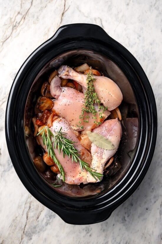 This Slow Cooker Coq au Vin is easier and lighter than the traditional version, but just as delicious with smoky bacon, mushrooms and onions. Ingredients added to slow cooker for coq au vin.