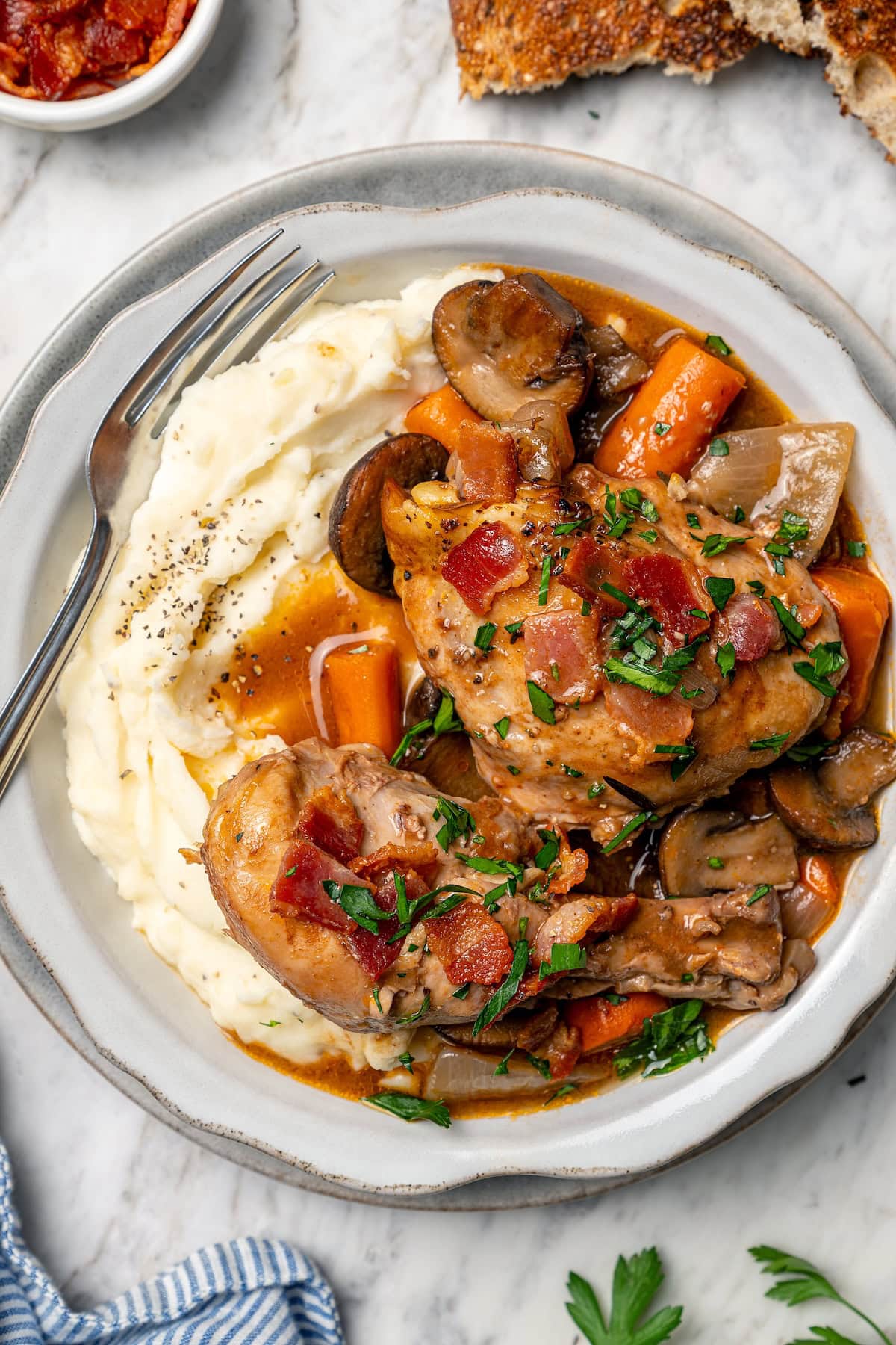 This Slow Cooker Coq au Vin is easier and lighter than the traditional version, but just as delicious with smoky bacon, mushrooms and onions. Crockpot coq au vin served over mashed potatoes.