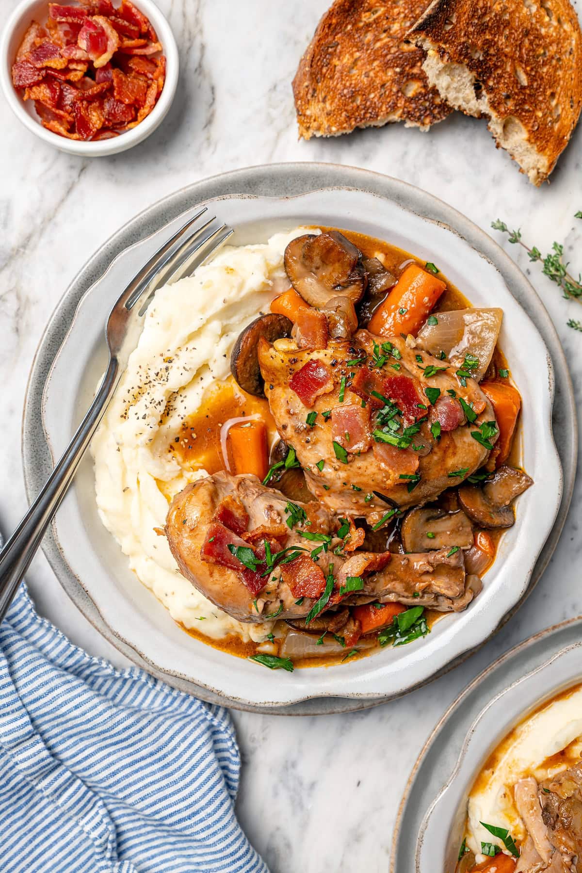 This Slow Cooker Coq au Vin is easier and lighter than the traditional version, but just as delicious with smoky bacon, mushrooms and onions. Bowl of mashed potatoes topped with slow cooker coq au vin.