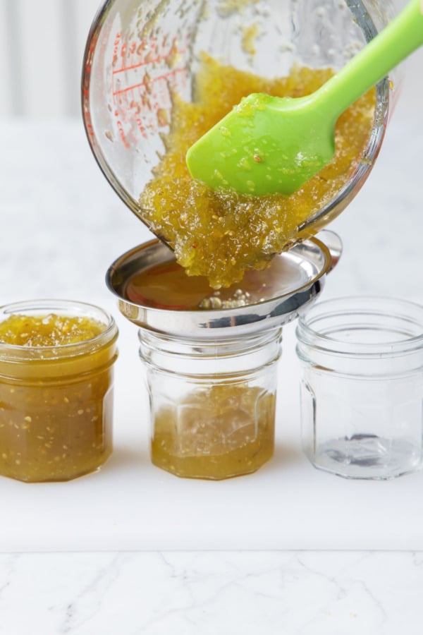Transferring green tomato jam to clean, sterilized canning jars with a jar funnel.