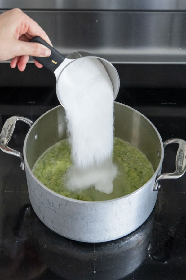 Pouring sugar into saucepan along with green tomato puree.