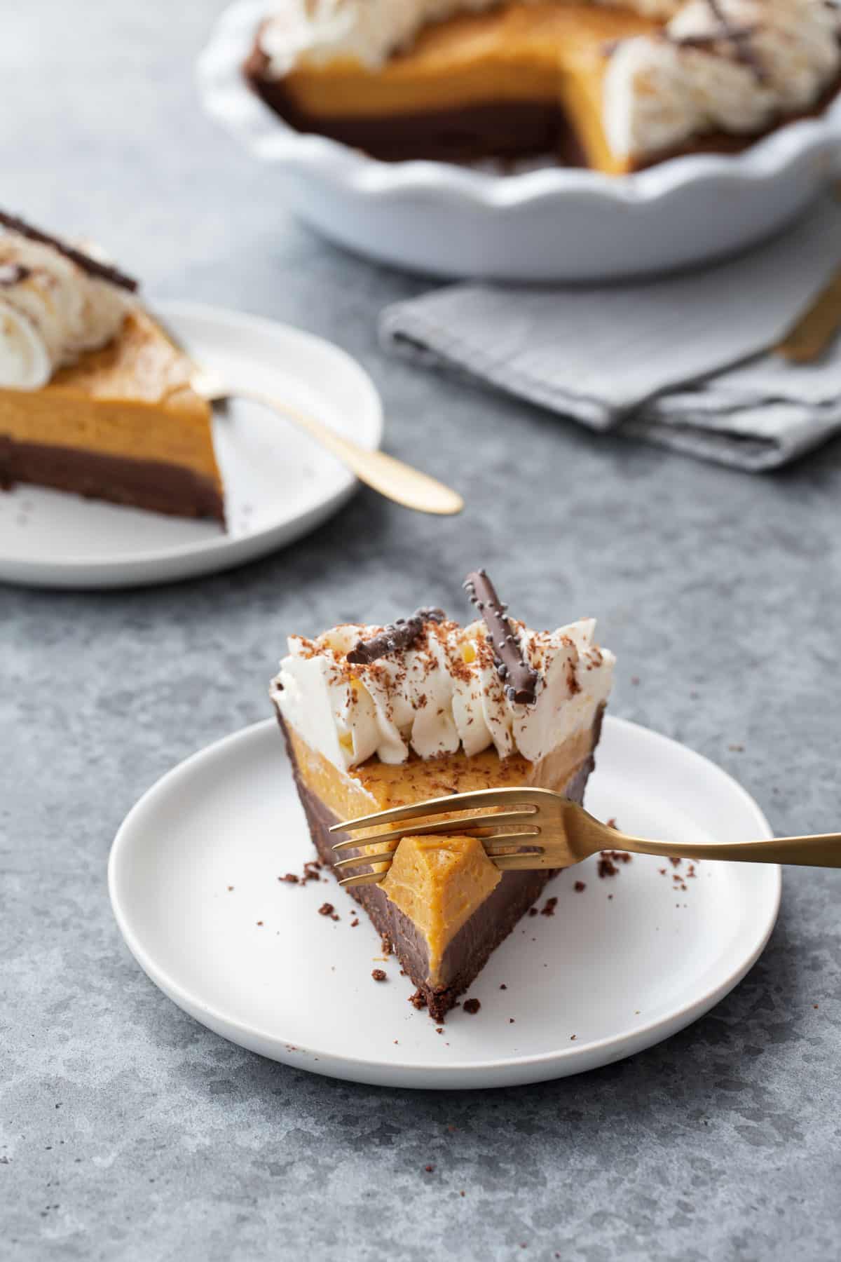 Fork cutting the tip off a slice of Black Bottom Pumpkin Cream Pie on a white plate with gray background.
