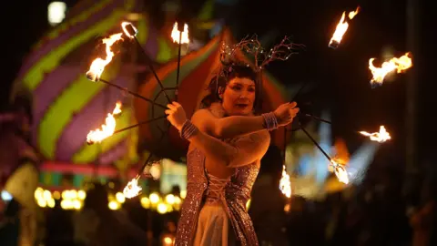 PA Media A street performer takes part in the Procession of Light in Dublin. She is holding  apparatus with fire on the end