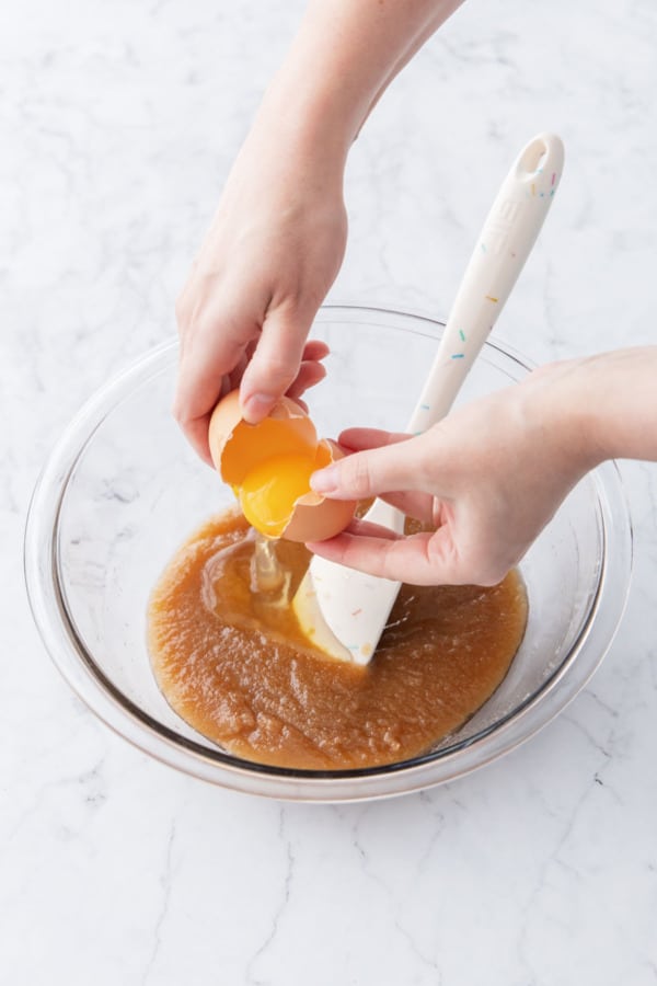 Cracking an egg into the sugar and melted butter mixture in a glass mixing bowl.