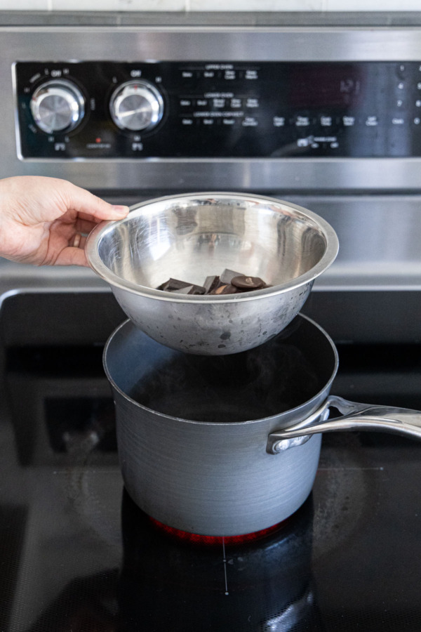 Placing a metal bowl on top of a saucepan of simmering water to form a double boiler.