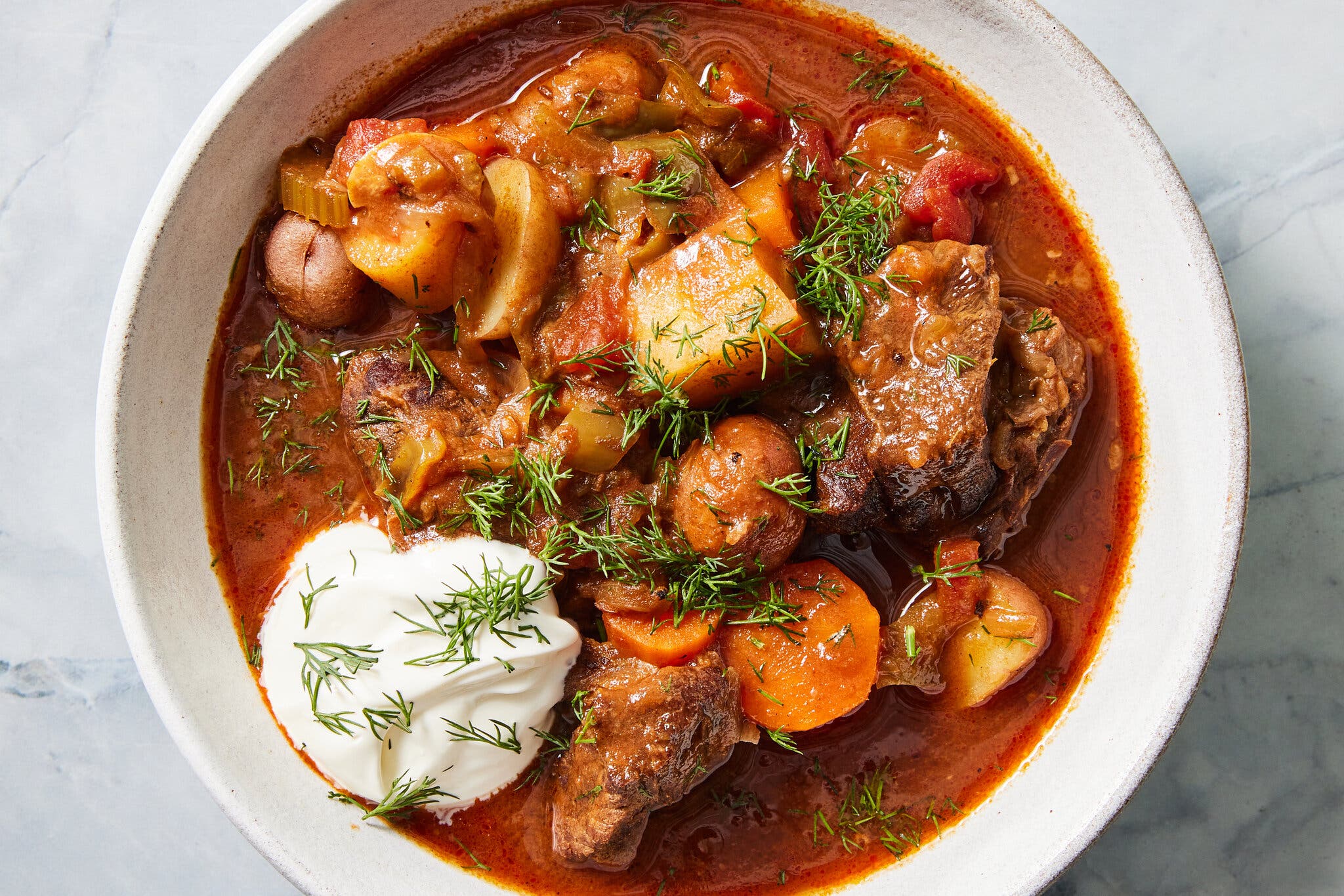 Tender beef, potatoes and carrots in a tomato-based broth, garnished with a swirl of sour cream and a generous sprinkling of chopped dill.