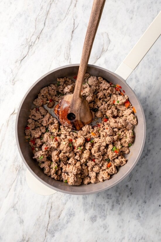 Browning turkey sausage in skillet with wooden spoon.