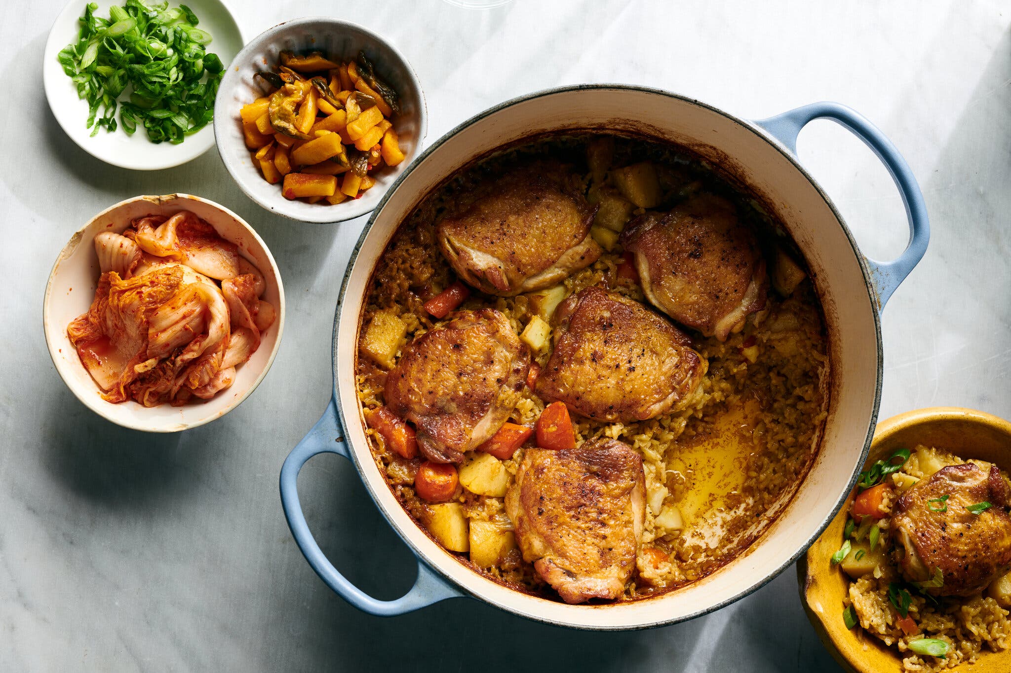 Roasted chicken thighs over seasoned rice in a blue Dutch oven.