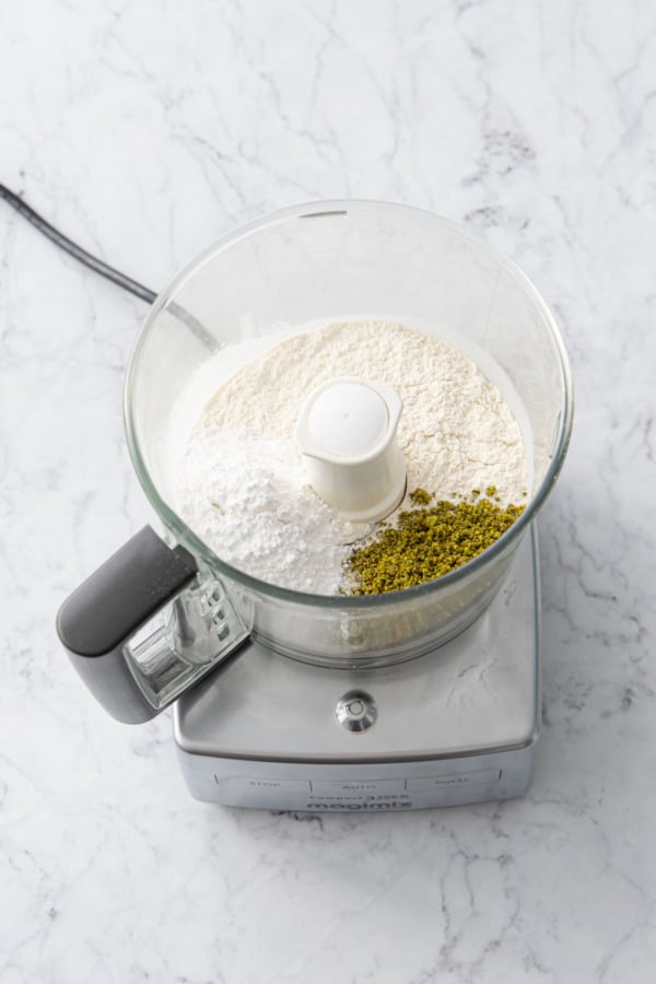 Food processor with flour, pistachios, and powdered sugar.