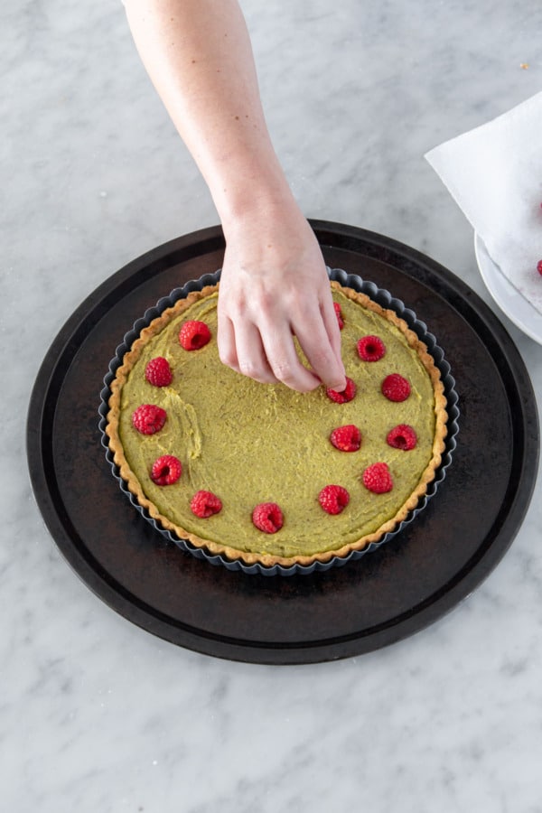 Pressing fresh raspberries into the pistachio frangipane filling before baking.